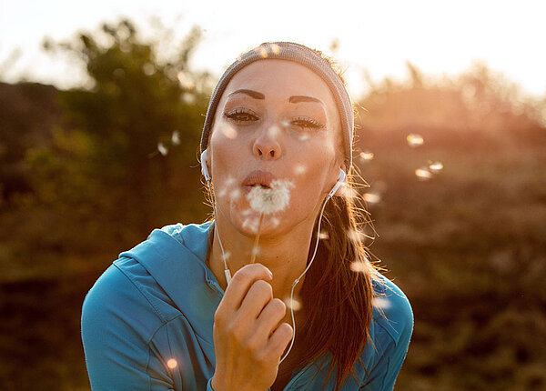 Glückliche Sportlerin bläst Pusteblume (Löwenzahn) 