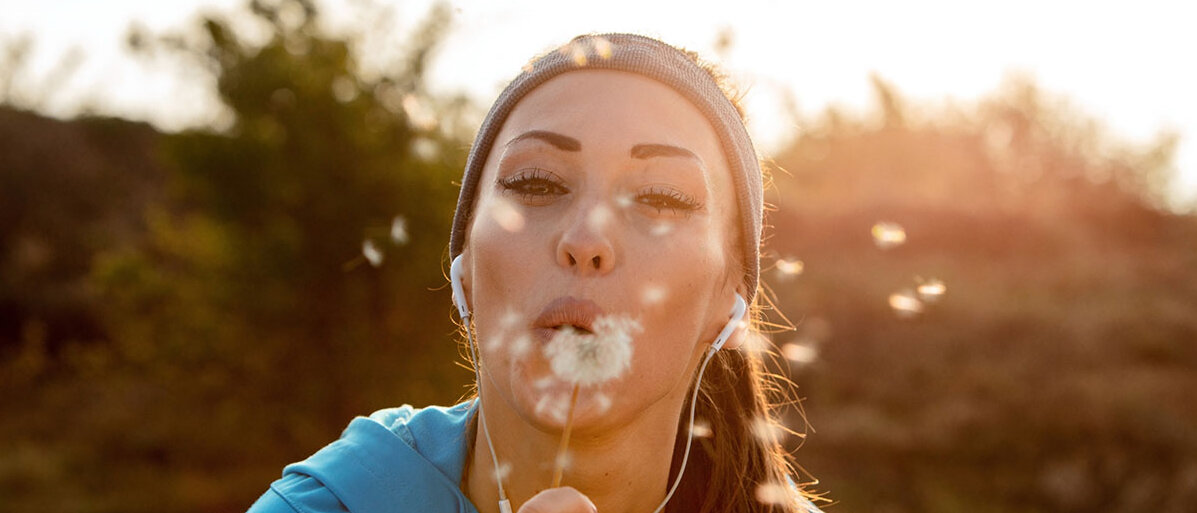 Glückliche Sportlerin bläst Pusteblume (Löwenzahn) 