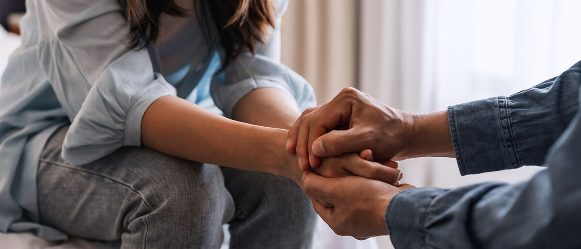 Der Unterschied zwischen Empathie und Mitgefühl Mann und Frau sitzend im Gespräch, die Hände aufeinandergelegt.