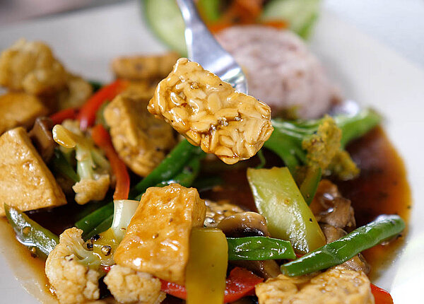 Gedünstete Tofustücke mit vielen grünen Bohnen, weißem Blumenkohl, Paprika und Reis in einer Soße.