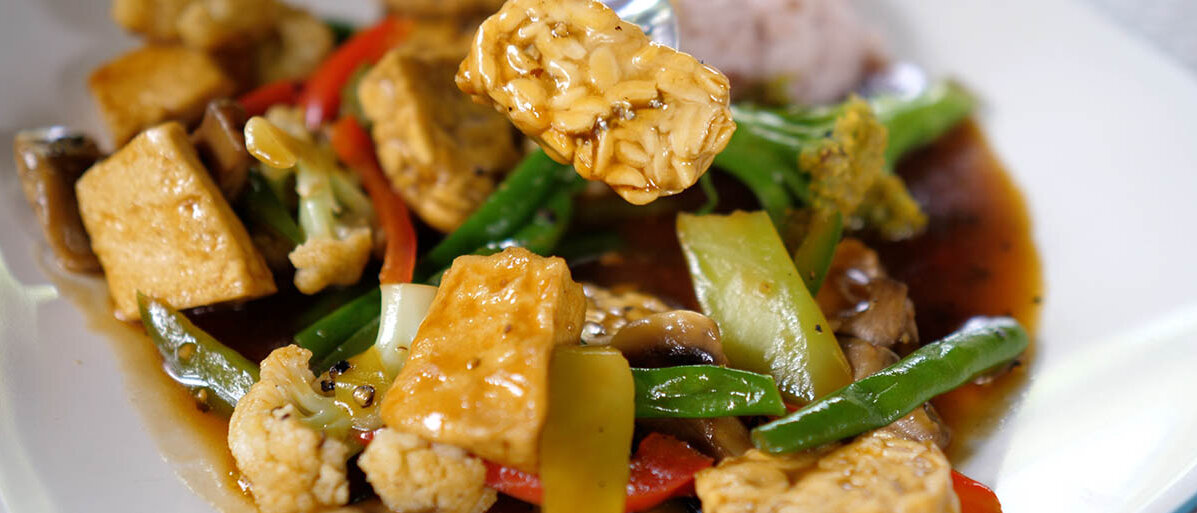 Gedünstete Tofustücke mit vielen grünen Bohnen, weißem Blumenkohl, Paprika und Reis in einer Soße.