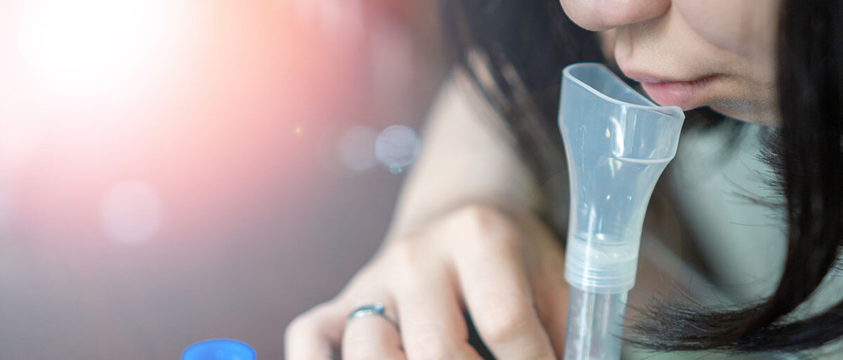Eine Frau hält ein Teströhrchen aus transparentem Kunststoff und spuckt hinein.