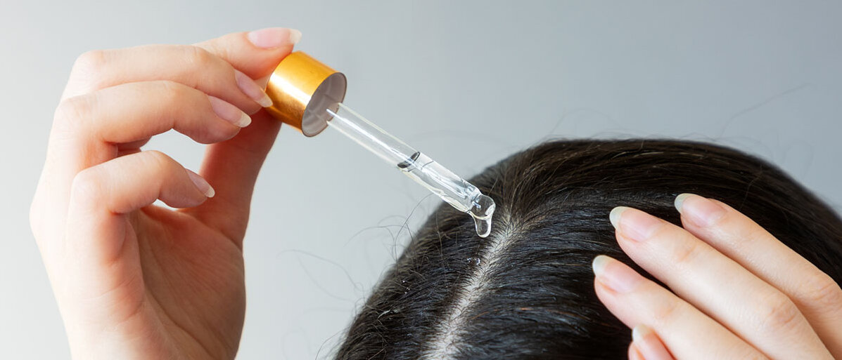 Eine Frau trägt Öl aus einer Pipette auf ihren Scheitel auf.