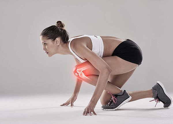 Eine Frau in Sportkleidung kniet in Startposition um loszurennen. In ihrem gebeugten Knie ist rot das Gelenk eingezeichnet.
