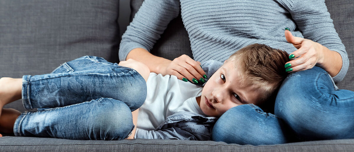 Ein kleiner Junge liegt bei seiner Mutter auf dem Schoß und hält sich den Bauch.