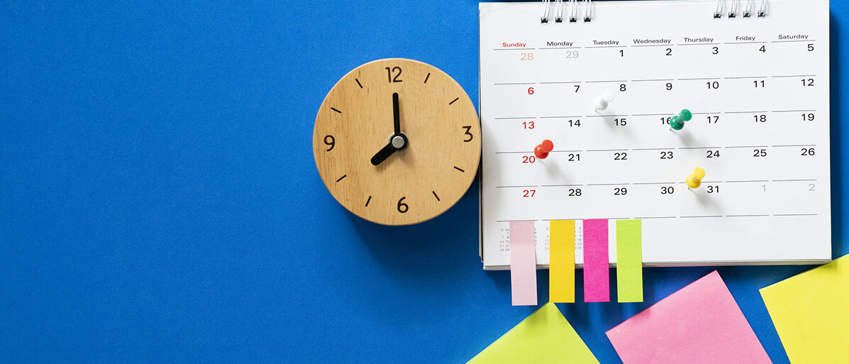 Nahaufnahme des Kalenders auf blauem Hintergrund mit Pins und Bleistift, der obendrauf liegt