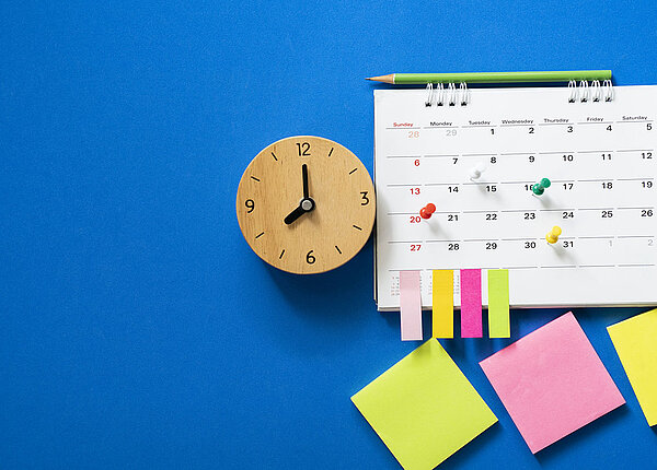 Nahaufnahme des Kalenders auf blauem Hintergrund mit Pins und Bleistift, der obendrauf liegt