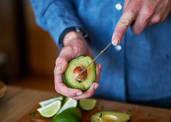 Avocado schneiden Mann hält Avocado in der Hand und schneidet sie auf