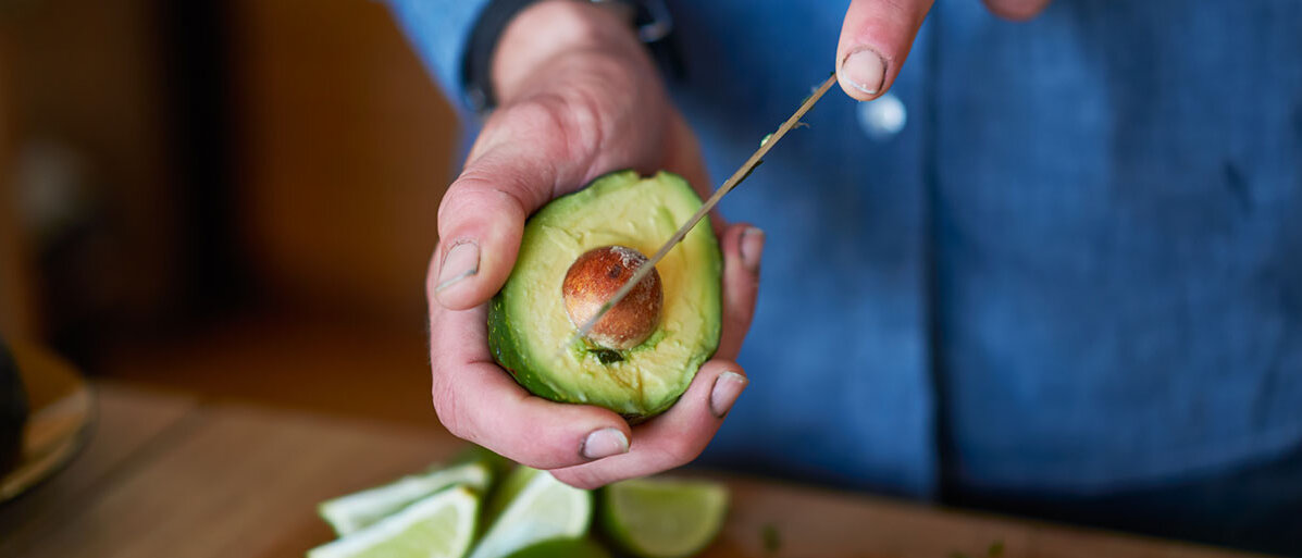 Avocado schneiden Mann hÀlt Avocado in der Hand und schneidet sie auf