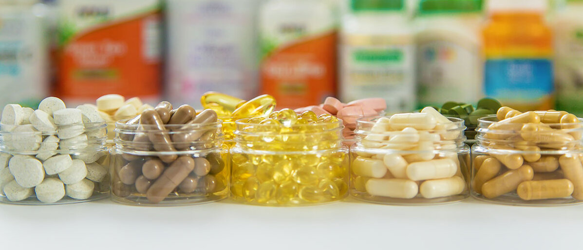Schälchen mit Nahrungsergänzungsmitteln und Vitaminen, im Hintergrund die Verpackungen dazu