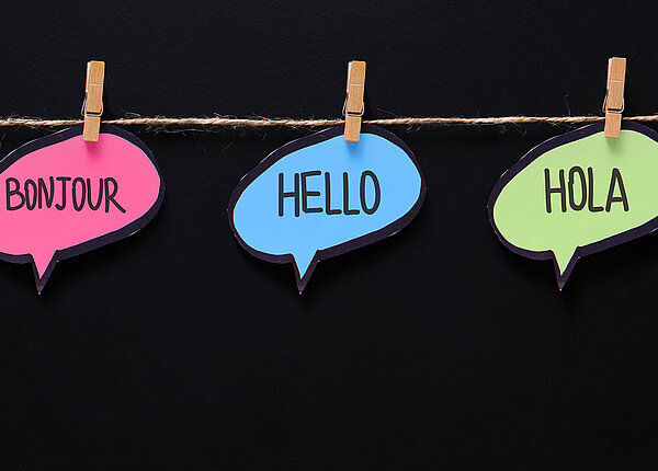drei unterschiedliche bunte Sprechblasen mit verschiedenen Sprachen aufgehängt an einem querverlaufenden Faden mit Holzklammern