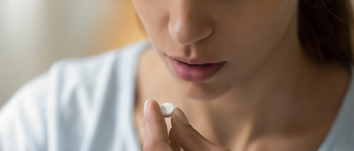 Frau hält sich Tablette vor den Mund
