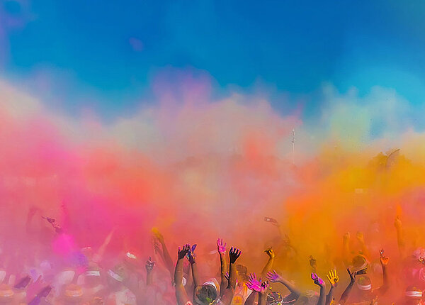 Eine Festival-Crowd (von hinten) wirft buntes Farbpulver in die Luft.