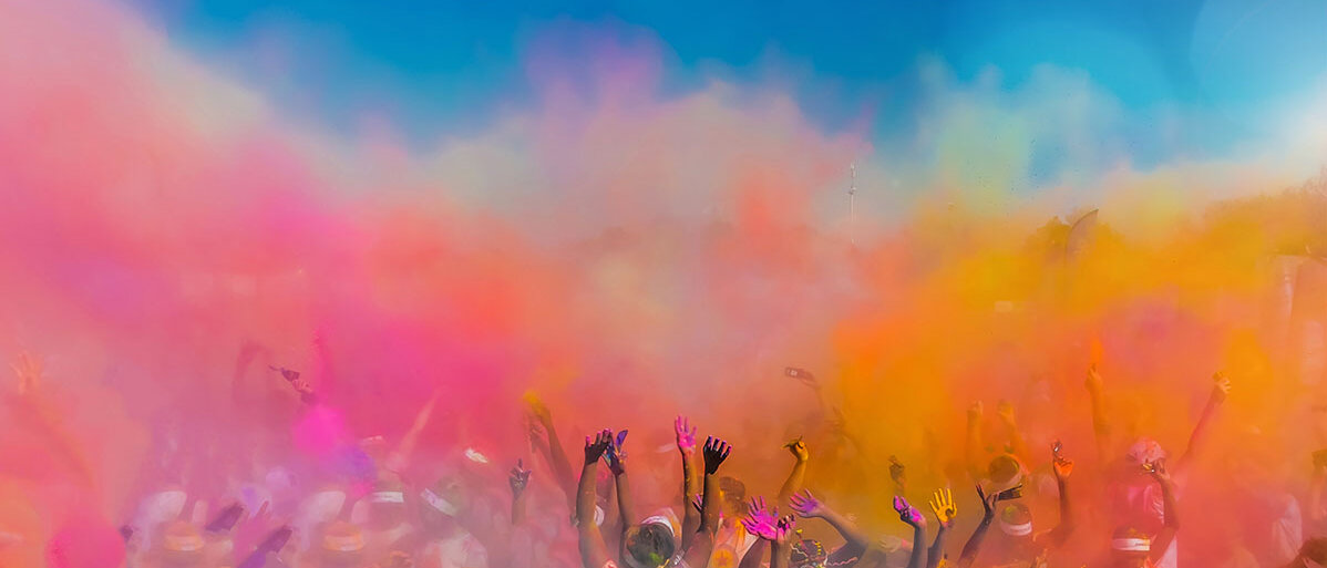 Eine Festival-Crowd (von hinten) wirft buntes Farbpulver in die Luft.