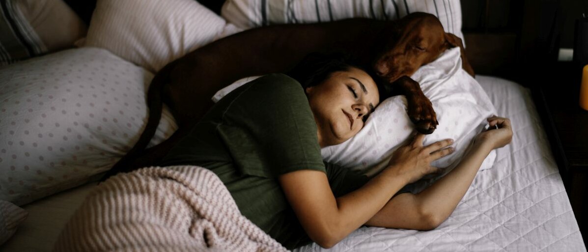 Frau und Hund schlafen entspannt zusammen im Bett