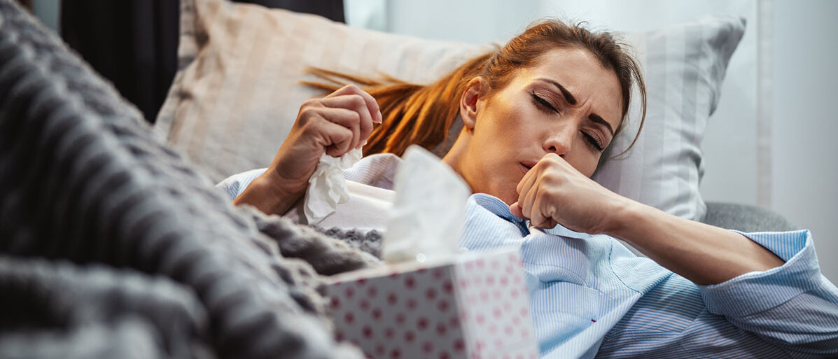 Gesundheit von Arbeitnehmenden Junge Frau im Pyjama im Bett. Sie hustet. Neben ihr eine Box mit TaschentĂĽchern.