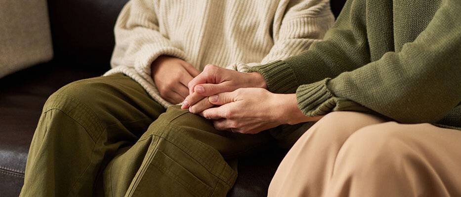 Depressionen betreffen auch das Umfeld zwei Frauen halten tröstend HÀndchen auf Couch