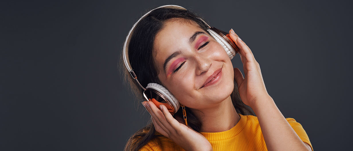 Junge Frau hat Kopfhörer auf, hört Musik, hat die Augen dabei geschlossen und lächelt.
