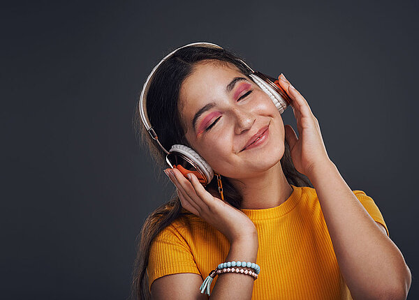 Junge Frau hat Kopfhörer auf, hört Musik, hat die Augen dabei geschlossen und lächelt.