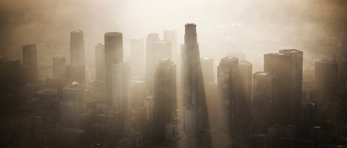Die Skyline von Los Angeles wird von der Sonne beschienen, dabei werfen die Hochhäuser lange Schatten in den Smog hinter ihnen.