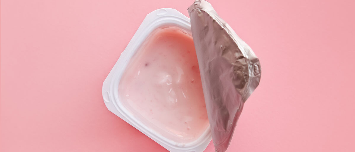 Geöffneter Joghurtbecher auf rosa Hintergrund