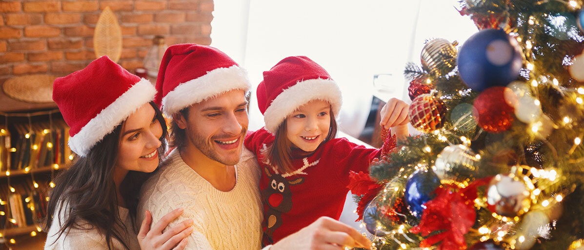Mutter, Vater und Tochter stehen am Weihnachtsbaum und haben rote Nikolausmützen auf