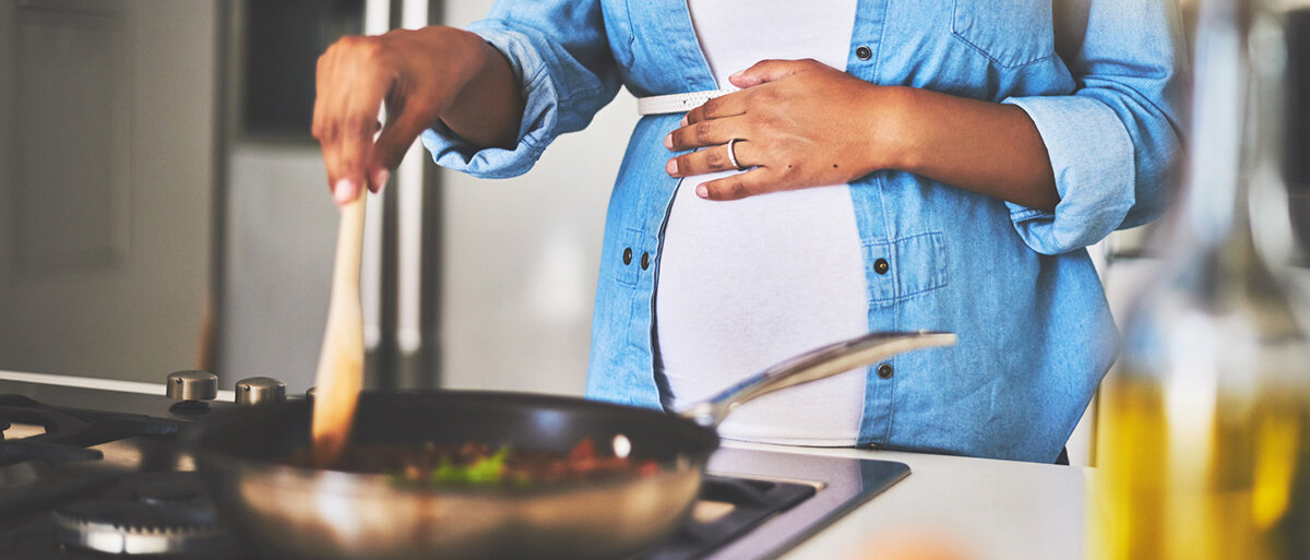 schwangere Frau kocht etwas mit einem Löffel in einer Pfanne