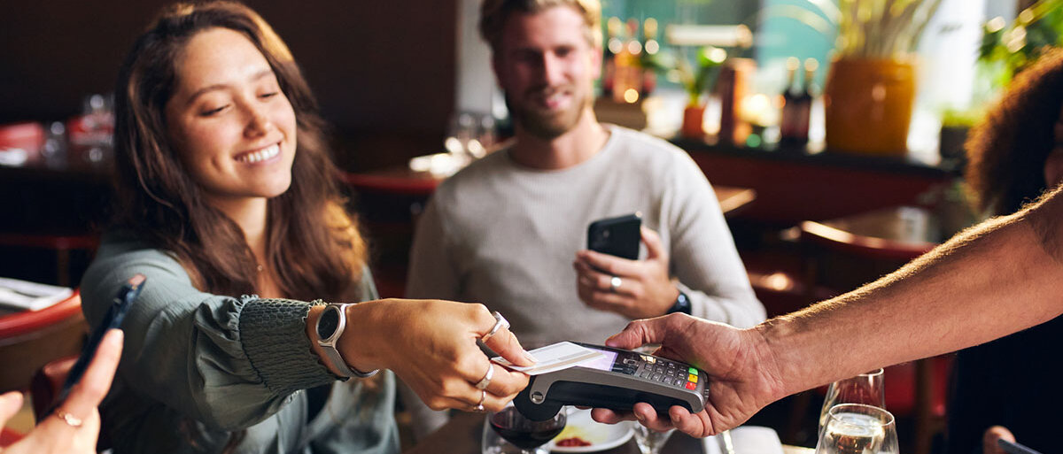 Gruppe von Freunden im Restaurant, in der Mitte eine Frau, die mit Karte bezahlt.