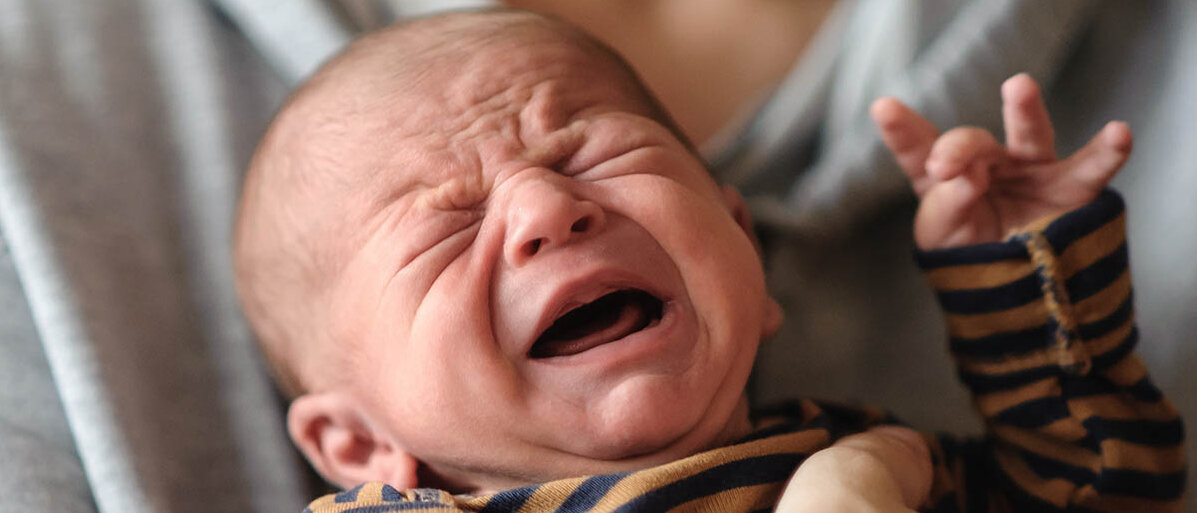 Hirnhautentzündung bei Neugeborenen entsteht durch gefährliche Darmkeime, aber Resistenzen gegen Antibiotika machen sie schwer behandelbar. Ein neugeborenes Baby wird im Arm gehalten und schreit.