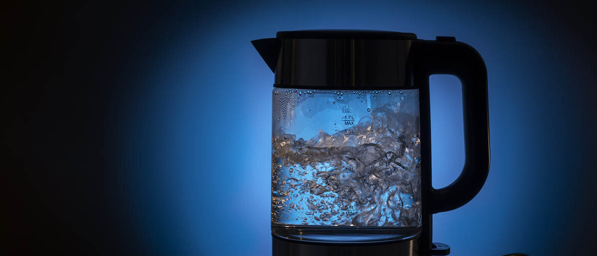 Umweltfreundlich und nachhaltig Kaffeemaschine und Wasserkocher entkalken In einem Wasserkocher aus Glas blubbert das Wasser.