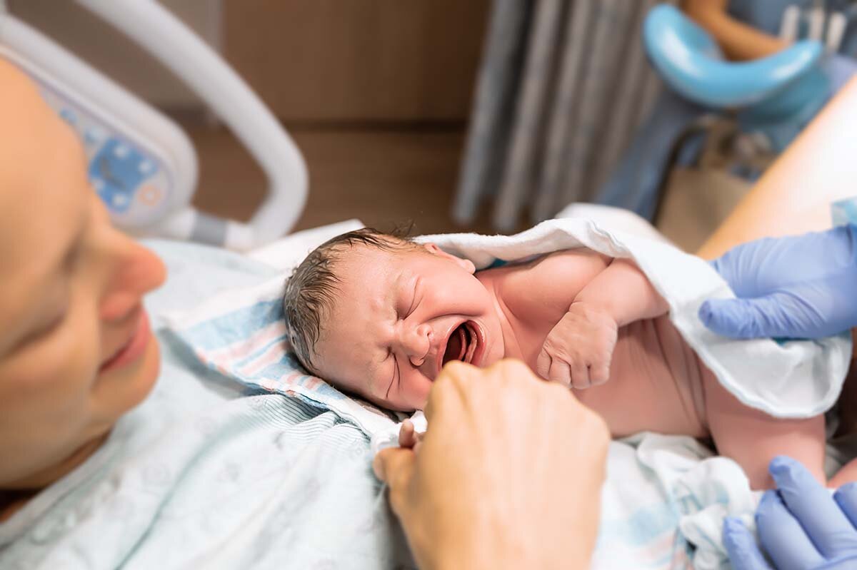 Eine Mutter liegt im Krankenhausbett und hält ihr neugeborenes, schreiendes Baby im Arm.