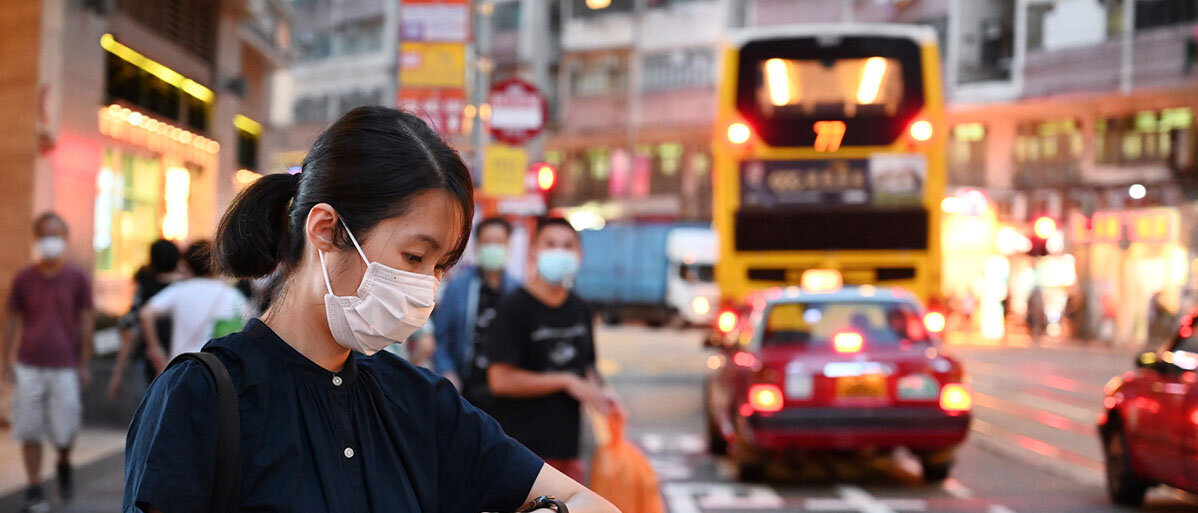 Junge chinesische Frau steht auf der Straße und schaut auf ihre Uhr
