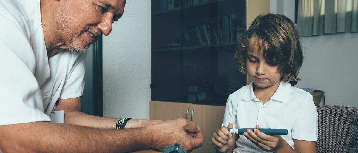 Ein Arzt zeigt und erklärt einem kleinen Jungen, wie er seinen Blutzuckerwert messen soll.