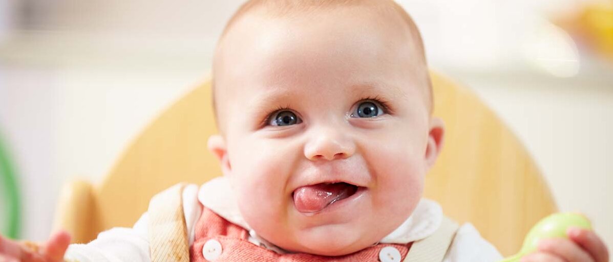 Porträt von einem glücklichen Baby mit einem bunten Plastik-Löffel in der Hand, das direkt in die Kamera schaut.