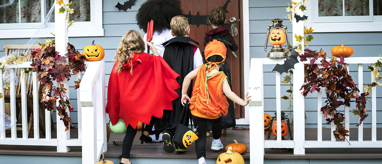 Kleine Kinder stehen Halloween verkleidet vor einer Haustür