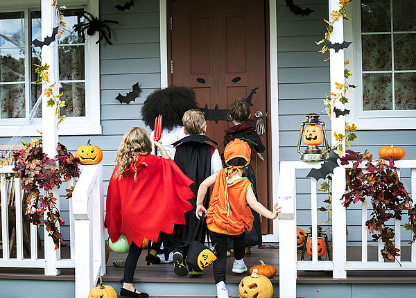 Kleine Kinder stehen Halloween verkleidet vor einer Haustür