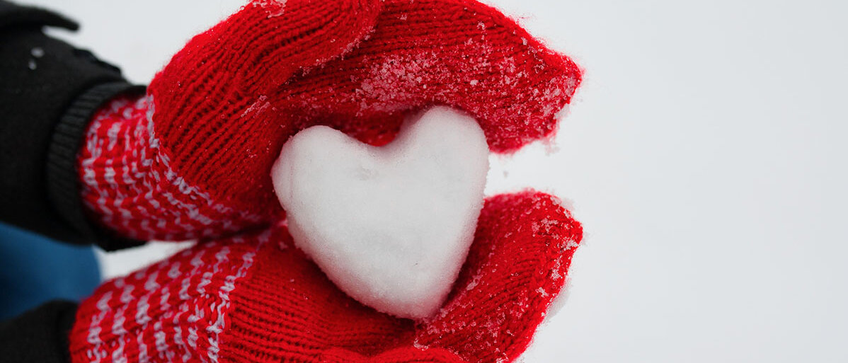 Haende mit roten Handschuhen halten ein Herz aus Schnee