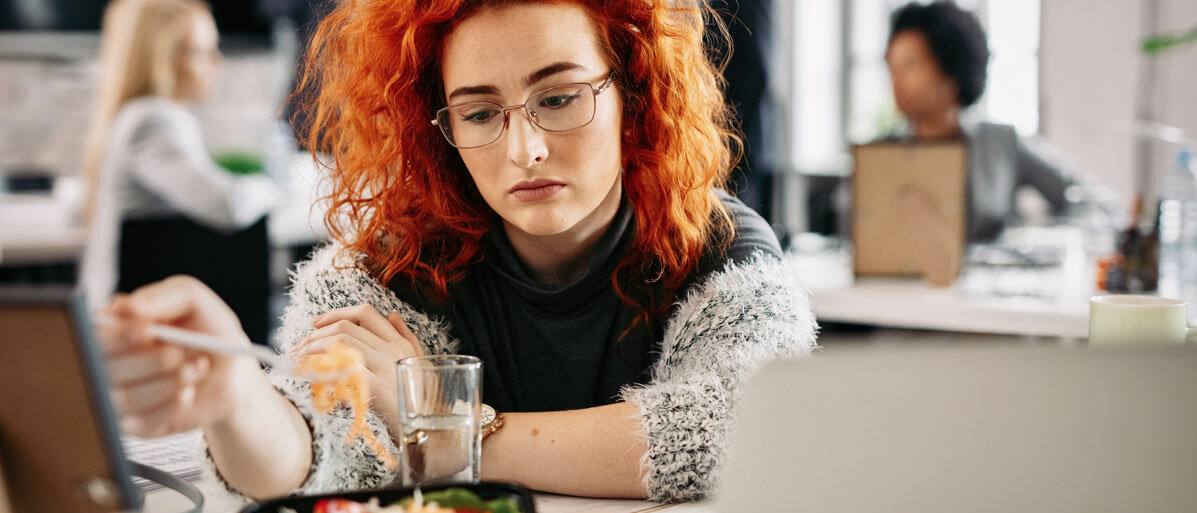 Eine junge Frau stochert lustlos in ihrem Mittagessen, sieht enttäuscht oder gelangweilt aus.