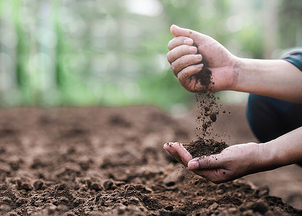 Eine Person, die auf dem Boden kniet, lässt eine Handvoll Erde durch ihre Finger rinnen.