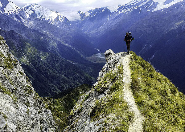 Wanderer mit Rucksack auf dem Ruecken wandert durch die Berge entlang einer Klippe