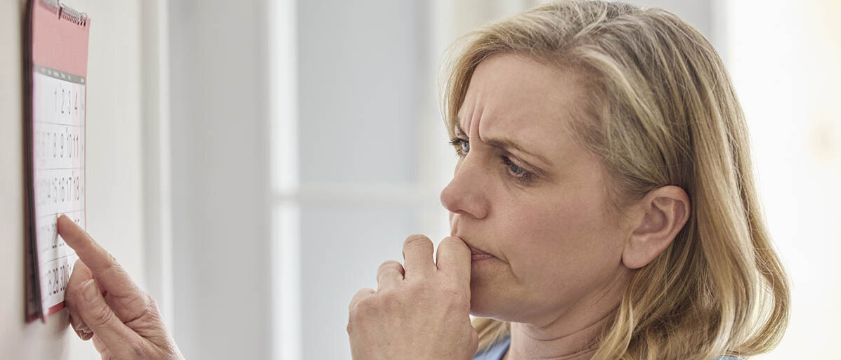 Wechseljahre und Östrogen: Das passiert während der Menopause mit den Östrogenrezeptoren. Eine Frau steht ratlos vor dem Kalender.