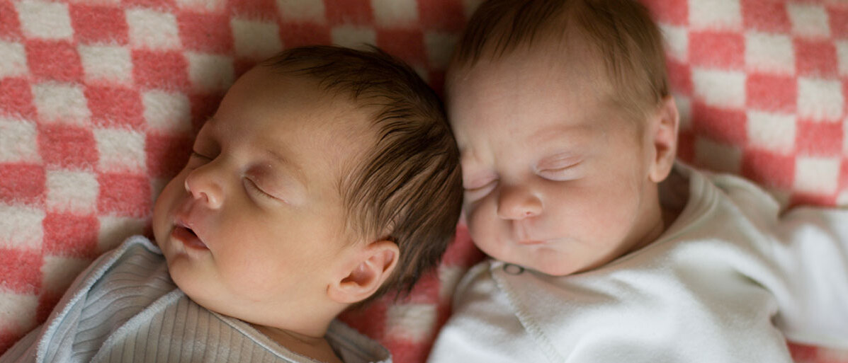 Zwei Babyzwillinge liegen schlafend nebeneinander.