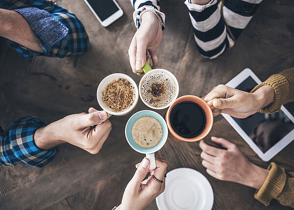 Kaffeekonsum in Deutschland Hochwinkelbild: vier Menschen strecken sich unterschiedliche Kaffeevarianten entgegen