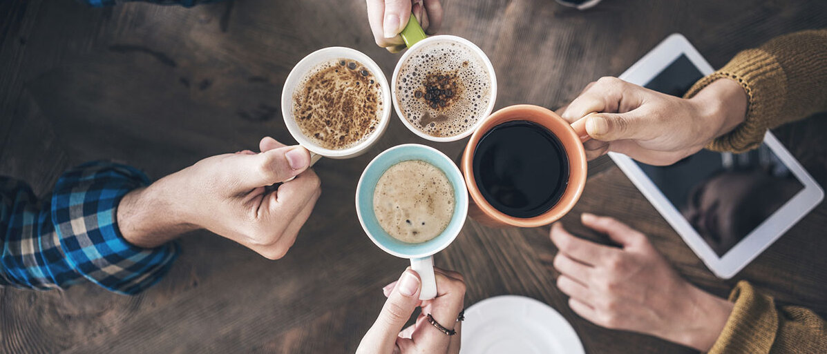 Kaffeekonsum in Deutschland Hochwinkelbild: vier Menschen strecken sich unterschiedliche Kaffeevarianten entgegen