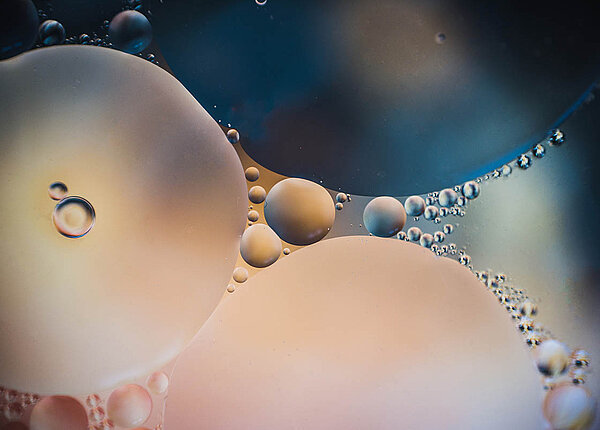 Emulsionen herstellen in der Rezeptur: Alles über Emulgatoren & Co. Zwei Flüssigkeiten, die sich nicht mischen, bilden große und kleine Tröpfchen aufeinander.