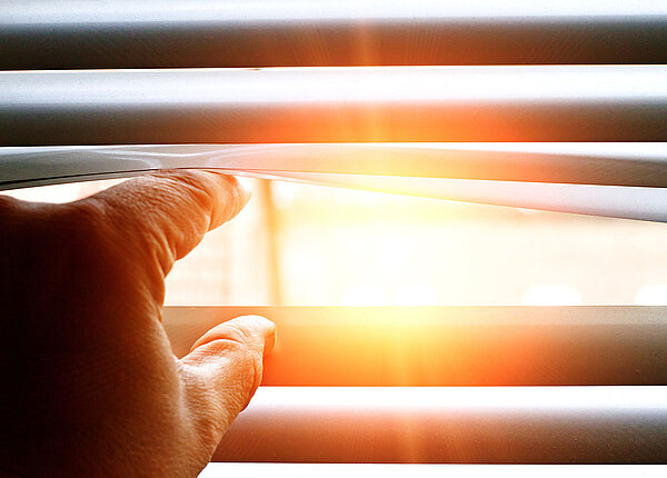 Hitze Finger schieben zwei Lamellen einer Jalousie auseinander, durch die die Sonne scheint