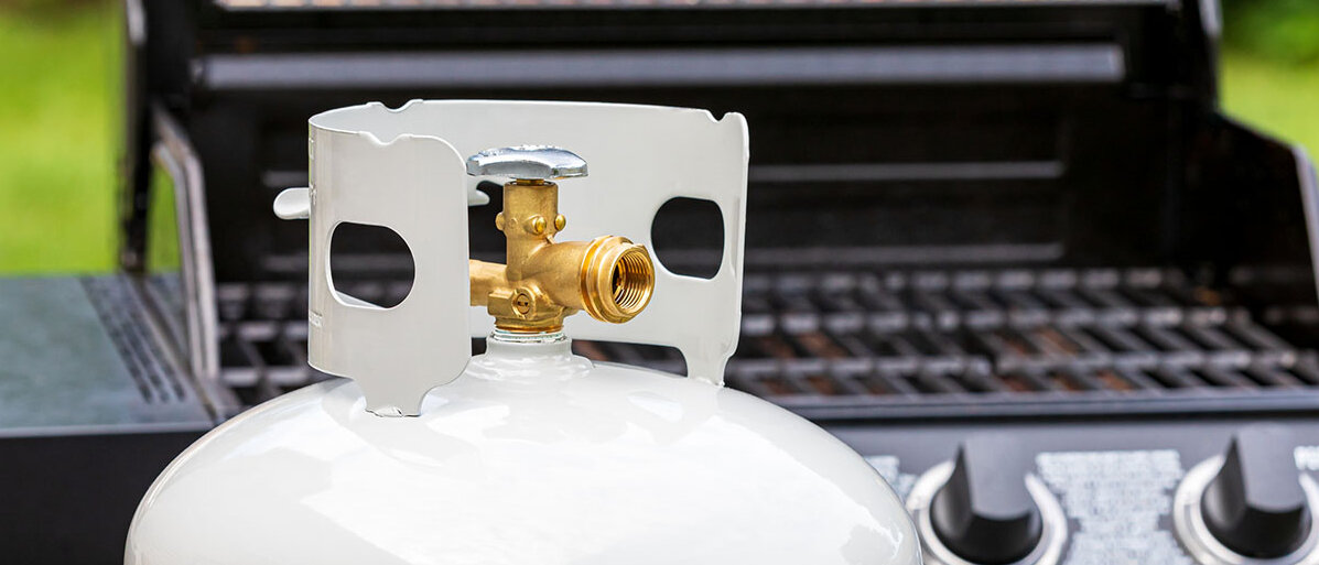 Eine weiße Gasflasche befindet sich vor einem Gasgrill.l