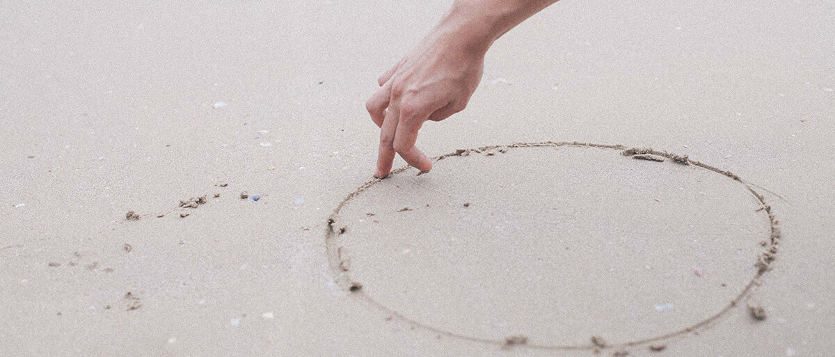 Eine Hand läuft einen in Sand gezeichneten Kreis ab