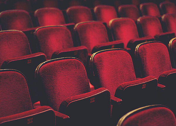 Mehrerere ansteigende Stuhlreihen, mit rotem Samt bezogen, eines Kinos oder Theaters.