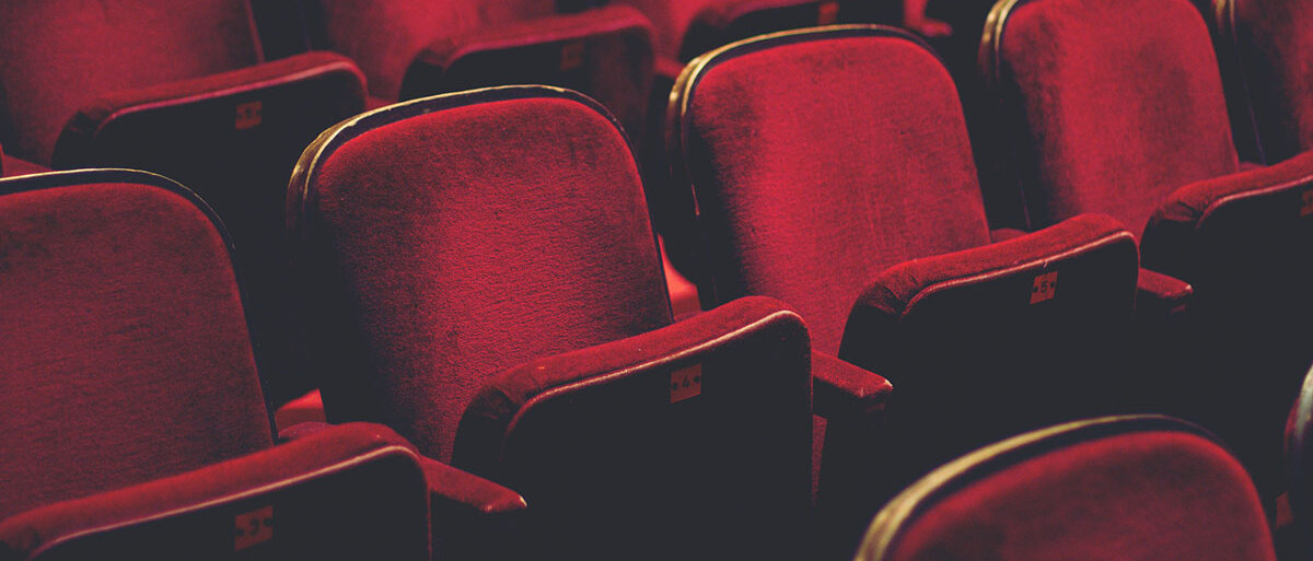 Mehrerere ansteigende Stuhlreihen, mit rotem Samt bezogen, eines Kinos oder Theaters.